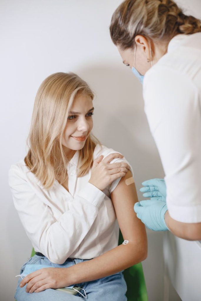 a-woman-with-band-aid-on-arm-6285397 A young woman smiles as she receives a vaccination from a healthcare professional wearing gloves.