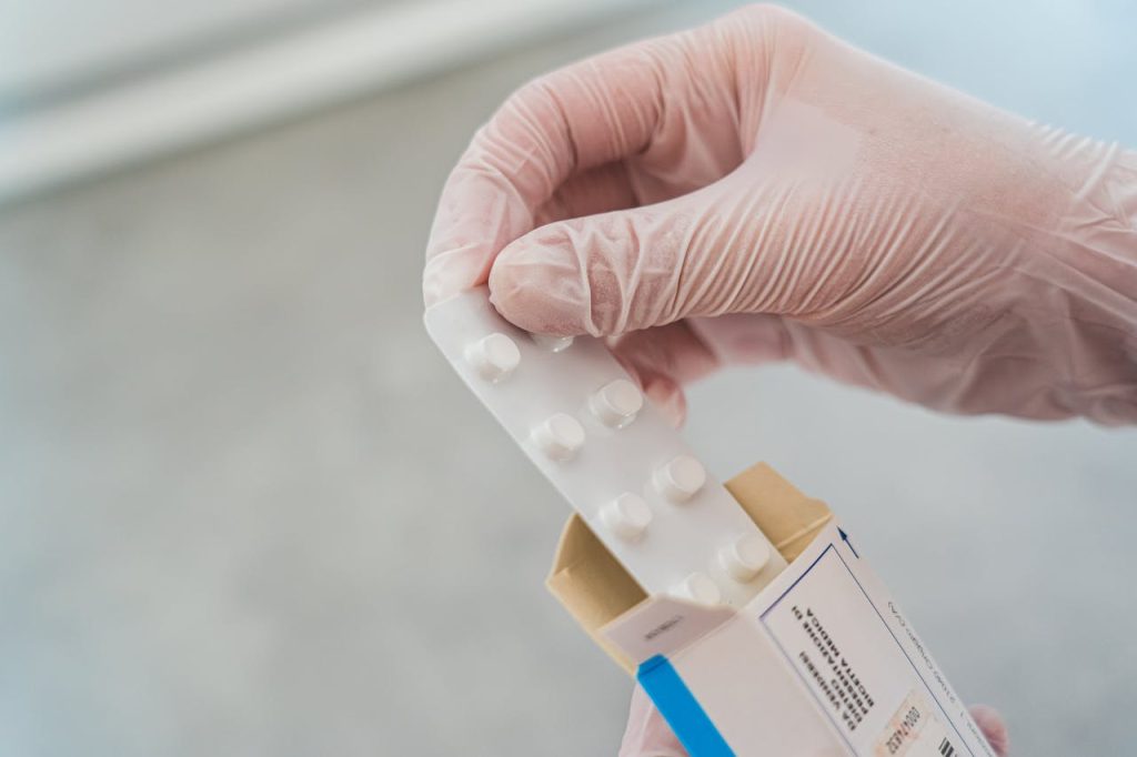 person-holding-white-and-blue-medicine-tablet-4058367 Close-up of a hand in gloves holding a blister pack of pills, symbolizing medical care.